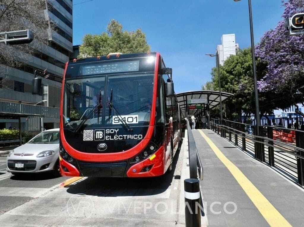 Metrobús eléctrico rojo y negro en estación elevada con plataforma de concreto en zona urbana