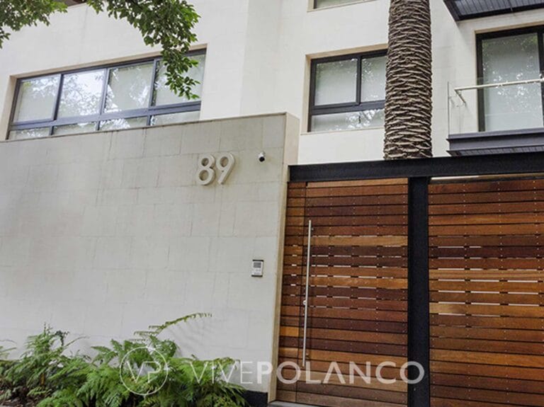 Fachada de casa moderna con muro de concreto, portón de madera horizontal y ventanas grandes con marcos negros en Calderón de la Barca 89, Polanco