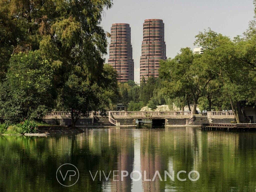 Vista de dos edificios residenciales de ladrillo rojo en Polanco desde un parque con lago y puente
