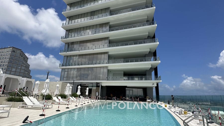 Spacious pool deck with white loungers and umbrellas at a luxury high-rise condo, overlooking the ocean.