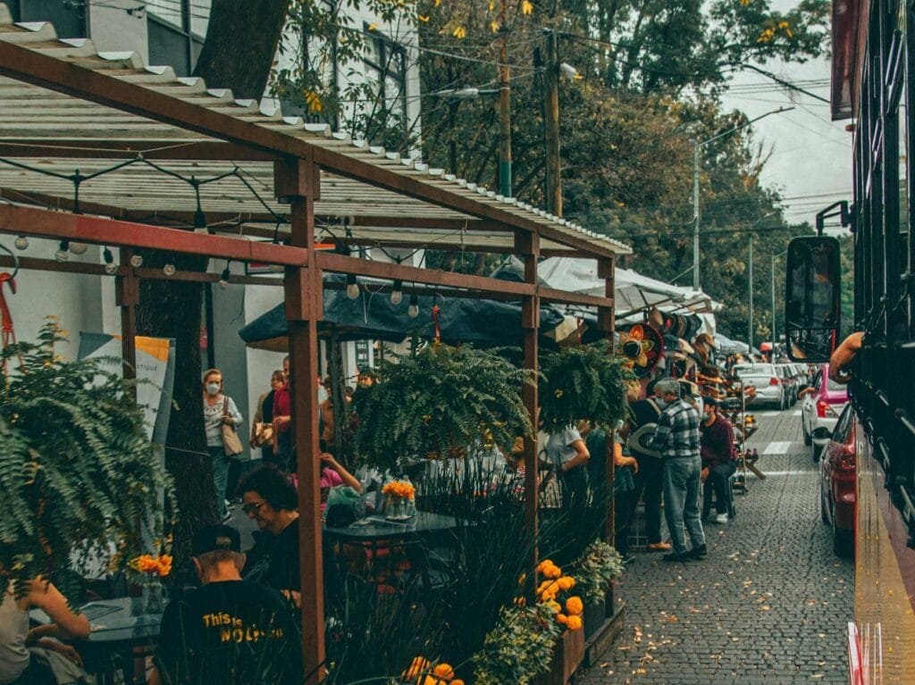 Calle empedrada con terrazas de restaurantes bajo pérgolas de madera y decoración floral naranja en Outside Cafe Flowers, Polanco