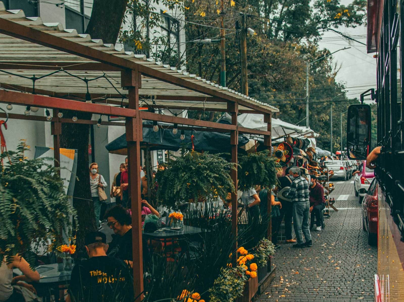 Calle empedrada con terrazas de restaurantes bajo pérgolas de madera y decoración floral naranja en Outside Cafe Flowers, Polanco