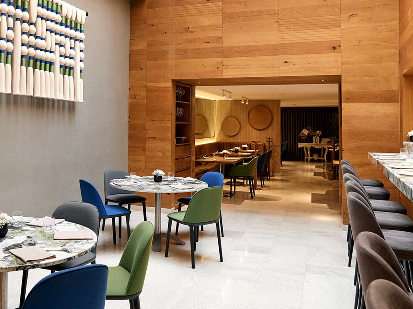 Comedor del restaurante Quintonil en Polanco con mesas de mármol, sillas de colores y paredes de madera