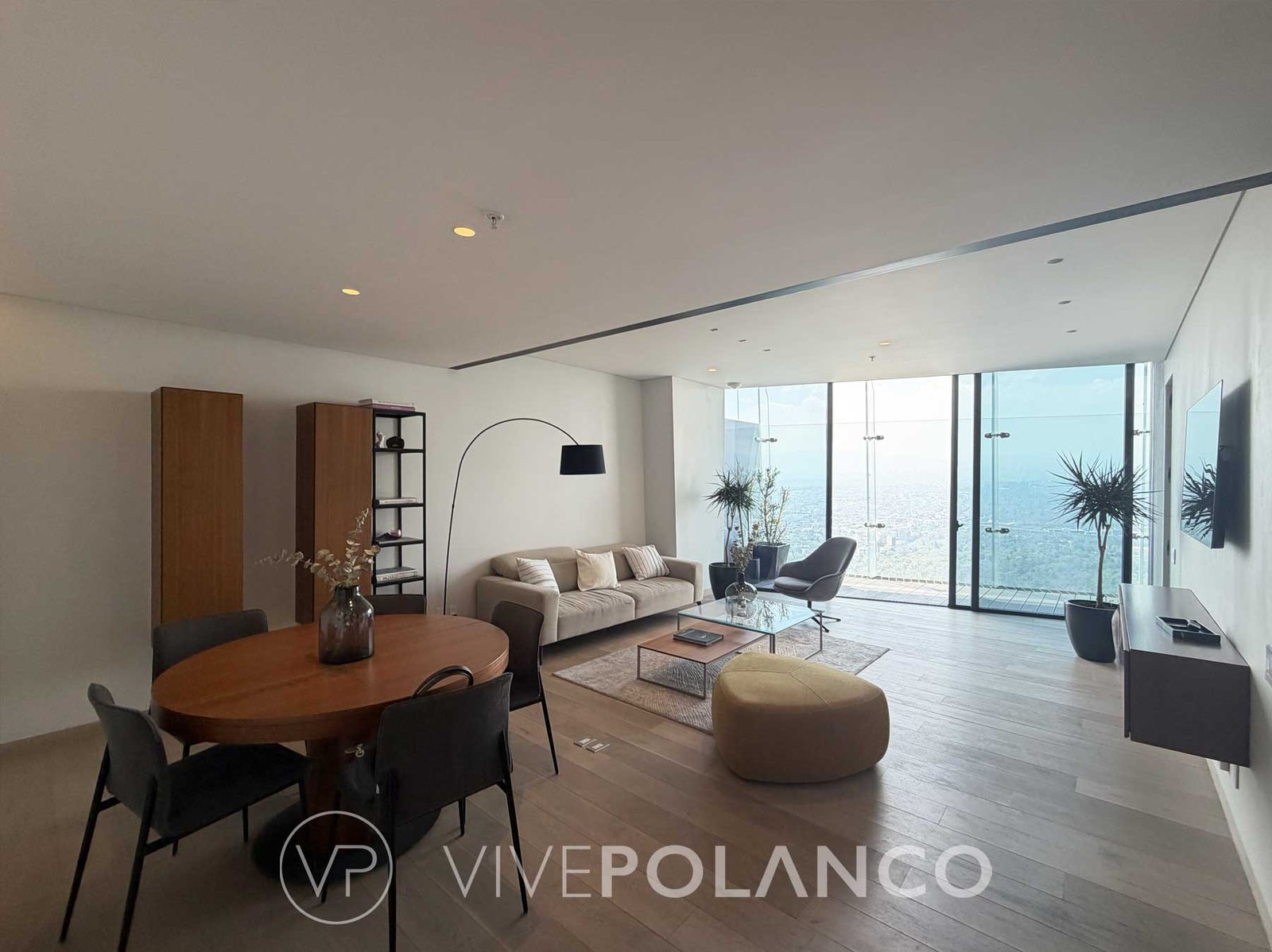 Sala de estar y comedor integrados con mesa redonda de madera, sofá beige y ventanales grandes en Ritz Carlton Cdmx, Polanco