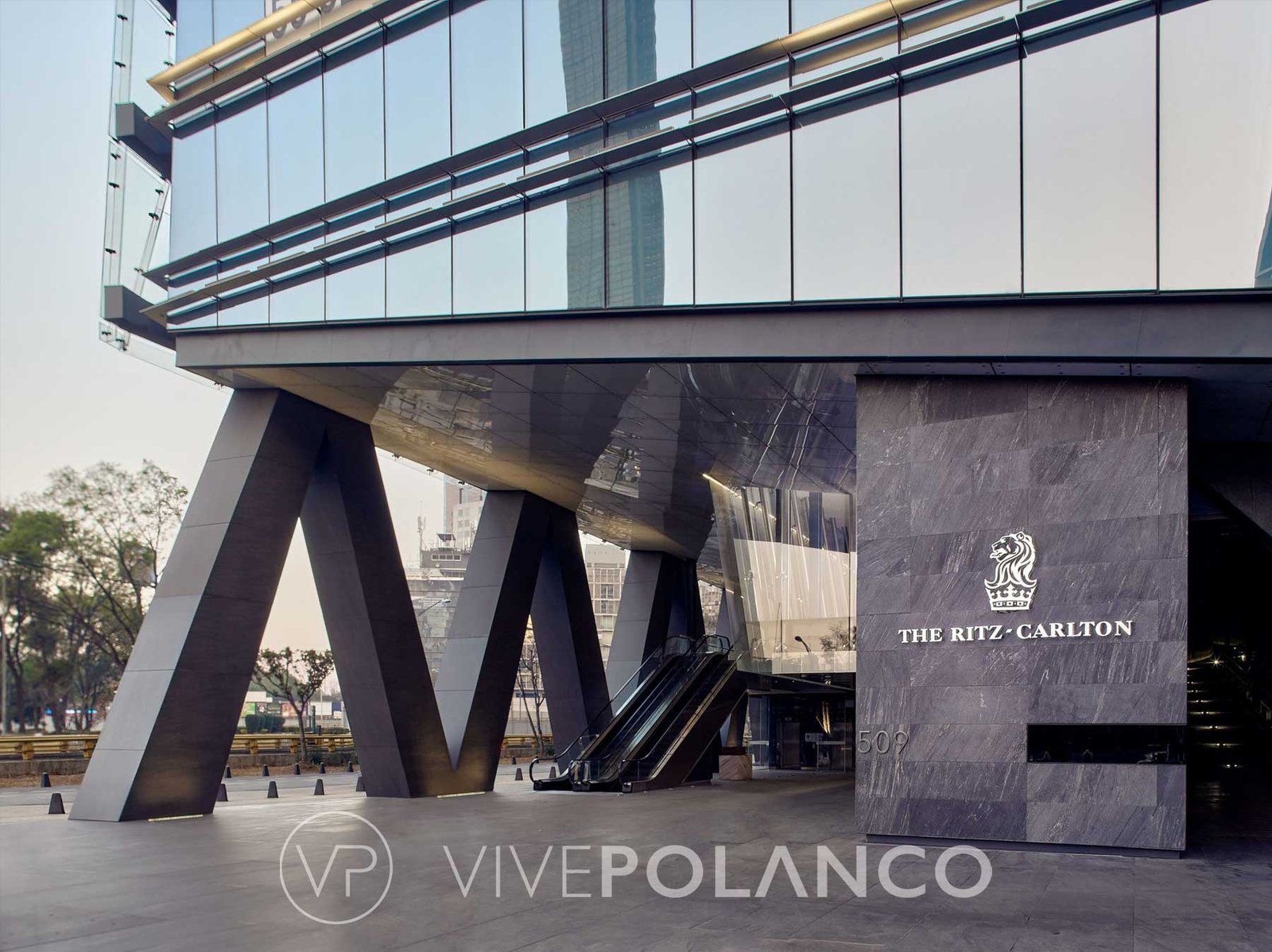 Entrada moderna de residencia de lujo con columnas inclinadas, escaleras eléctricas y fachada cristal en Ritz Carlton Cdmx7, Polanco