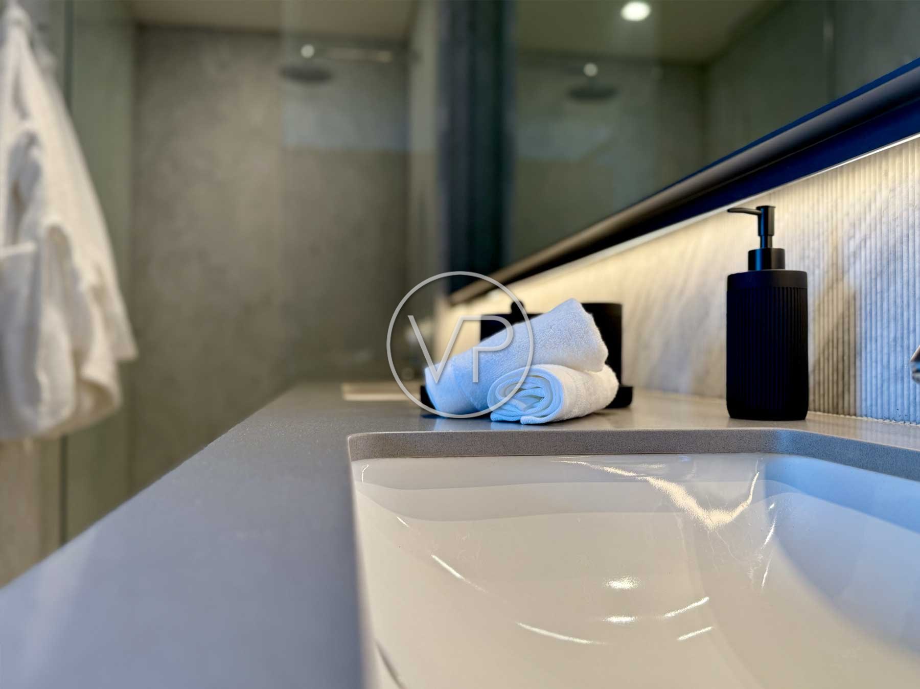 Lavabo empotrado con toallas enrolladas, dispensador negro y luz LED bajo el espejo en Polanco
