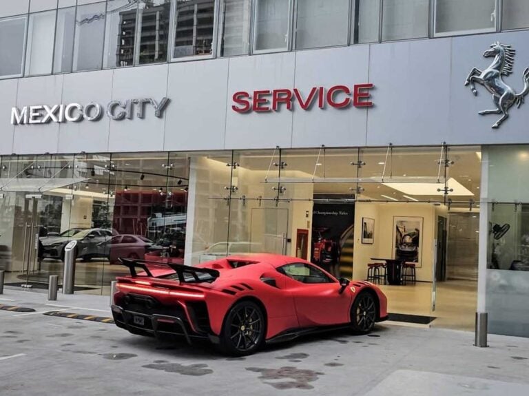Automóvil deportivo rojo estacionado frente a agencia automotriz con fachada de vidrio y showroom visible