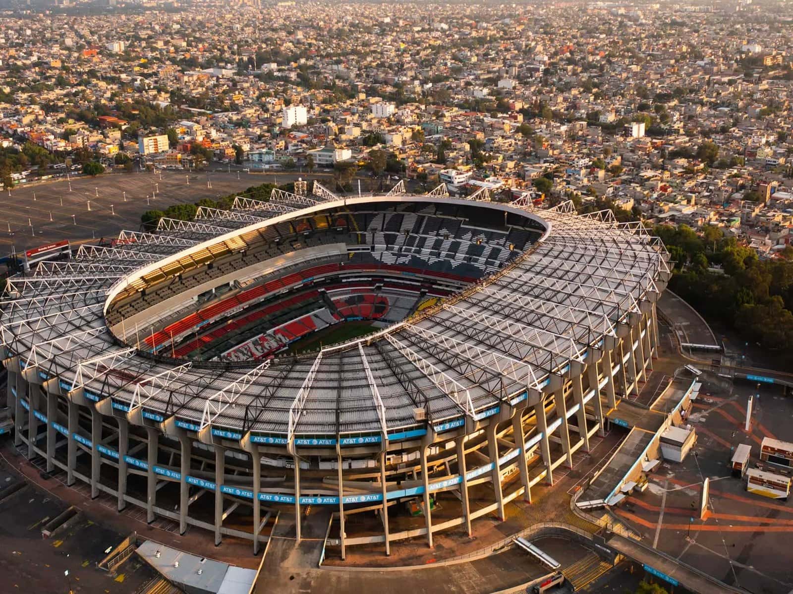 Vista aérea del Estadio Azteca con arquitectura circular moderna y la ciudad de México al fondo durante el atardecer