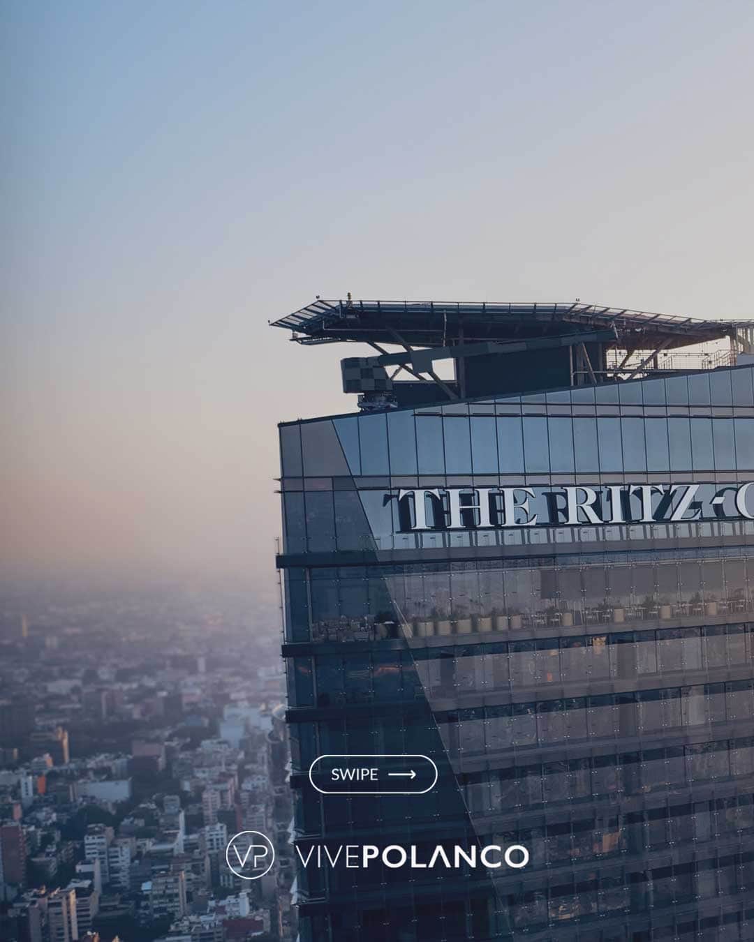 Vista aérea de edificio residencial de lujo con fachada de cristal y helipuerto en la azotea durante el atardecer