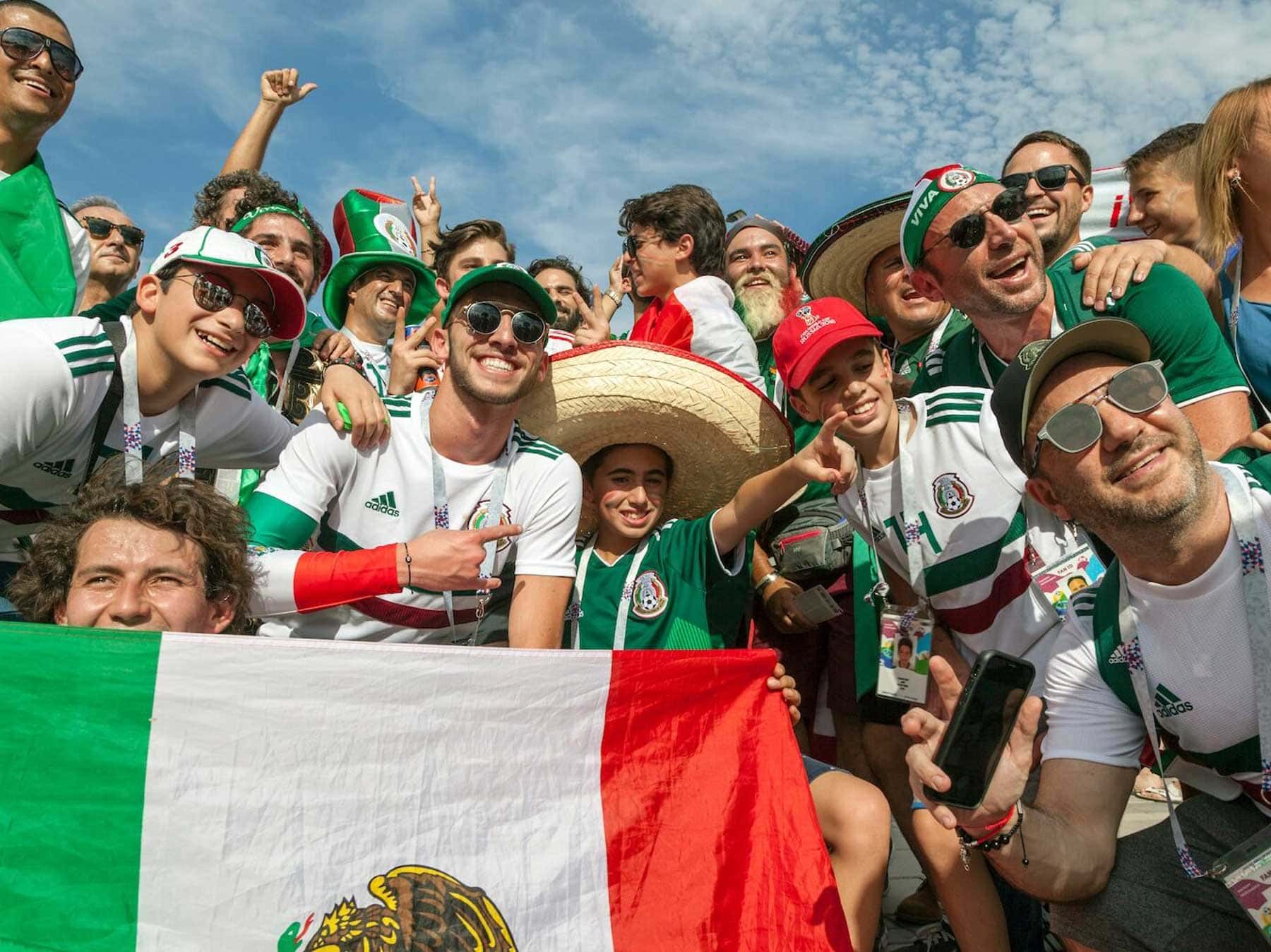 Aficionados mexicanos celebrando en las gradas con bandera de México, sombrero y camisetas verdes durante el Mundial