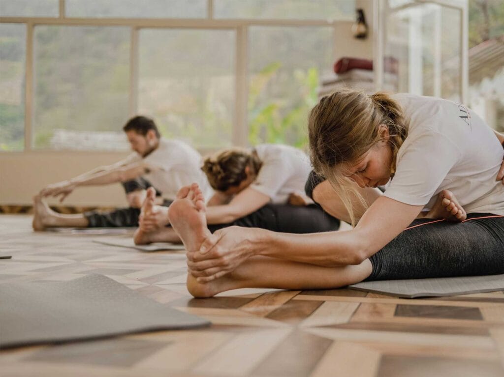Tres personas practicando yoga en estudio luminoso con piso de madera y grandes ventanales